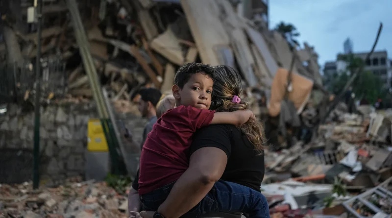 Niño en brazos de su madre frente a los escombros de un edificio residencial colapsado tras el doble terremoto en Venezuela de 2026.
