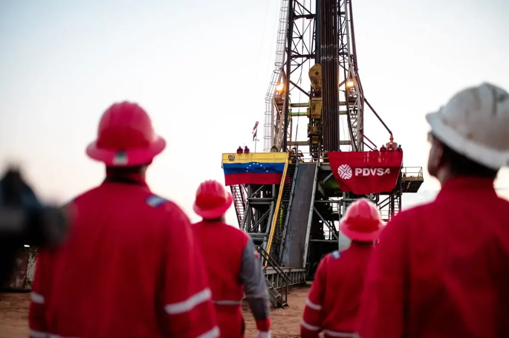 Trabajadores de PDVSA en un campo petrolero con un torre con la bandera de PDVSA y de Venezuela