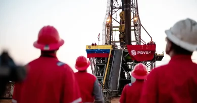 Trabajadores de PDVSA en un campo petrolero con un torre con la bandera de PDVSA y de Venezuela